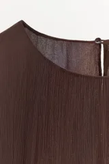 Vestido midi de viscosa color marrón, con cuello redondo, mangas largas amplias y diseño holgado. Presenta bordados en relieve con aplicación de abalorios a tono en el frente.