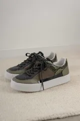 Championes urbanos con diseño de paneles en tonos verde oliva, negro y gris. Presentan una combinación de texturas que incluye cuero liso, gamuza y un panel con estampado de piel de serpiente en el talón. Cuentan con cordones negros y una suela de plataforma blanca con textura acanalada.