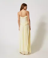 Vestido largo color amarillo pálido, confeccionado en georgette con rayas de raso. Cuenta con tirantes finos, escote de pico decorado con volantes y falda fruncida de corte redondeado en la cintura. Prenda forrada, de corte holgado.
