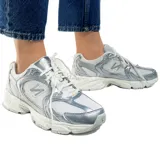 Championes urbanos New Balance modelo 530, con diseño inspirado en el running clásico. Presentan una combinación de malla blanca y revestimientos sintéticos en color plateado metálico, con el logo N característico en los laterales y entresuela con tecnología ABZORB para mayor amortiguación.