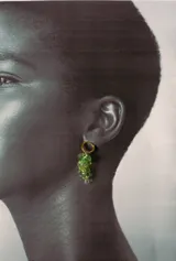 Aro tipo argolla dorada con colgante en forma de racimo de uvas, compuesto por pequeñas cuentas de cristal verde y hojas metálicas doradas.