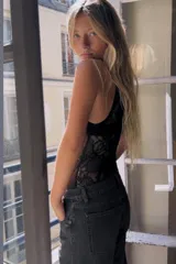Body negro confeccionado en encaje semitransparente, con diseño sin mangas y cuello halter alto con detalle de tejido plisado. Cierre inferior con broches a presión.