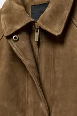 Chaqueta oversize confeccionada en piel de ante, con cuello solapa, manga larga con puños elásticos y bajo elástico. Presenta bolsillos de plastrón con solapa en el frente y cierre frontal con cremallera y botones ocultos.