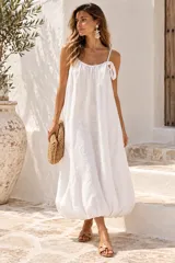 Vestido largo blanco de lino, con tirantes finos, escote redondo fruncido con detalle de lazo en el hombro y diseño de falda abombada en el ruedo.
