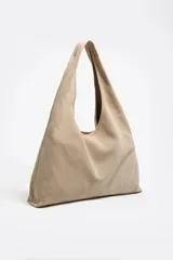 Bolso de hombro maxi de estructura blanda, exterior de serraje color beige claro, con cierre de cordón y logo metálico.