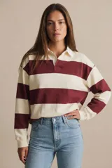 Sweater estilo polo de corte oversize, con diseño de rayas horizontales anchas en color bordó y crema. Presenta cuello camisero con cierre de botones y mangas largas con puños elásticos.