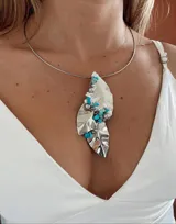 Collar rígido plateado con dije de alpaca con forma de hoja irregular, decorado con piedras turquesas, perlas y cuentas plateadas.