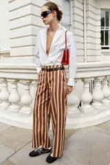 Pantalón de tiro alto y pernera recta con estampado de rayas verticales en tonos azul, marrón y beige. Incluye un cinturón delgado de color marrón oscuro con hebilla metálica dorada.