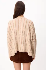 Sweater de punto con diseño de trenzas verticales, cuello redondo y corte crop. Presenta una combinación de colores crudo y camel, con mangas largas y ajuste holgado.