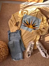 Sobre camisa de pana color amarillo, de manga larga, con botones forrados y un gran parche rectangular en la espalda con diseño de sol bordado en tonos tierra y azul claro.