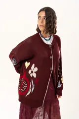 Saco de punto color vino con diseño holgado, cuello redondo y mangas largas. Presenta un gran bordado central en la espalda con forma de flor en tonos crema y rojo, acompañado de un pequeño bordado de sol y una frase bordada en la parte inferior.