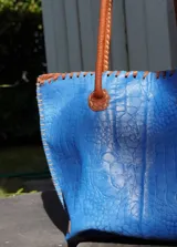 Bolso shopper de cuero azul con textura crocco, manijas largas marrones y costuras artesanales visibles en los bordes.
