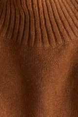 Buzo oversized de punto suave con cuello tortuga acanalado y abertura en la nuca. Presenta mangas raglán con costuras decorativas y terminaciones acanaladas en puños y bajo.