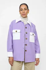 Sobre camisa de corte holgado en combinación de colores lila y blanco. Presenta cuello clásico, cierre frontal con botones, dos bolsillos frontales con solapa y puños en contraste.