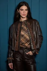 Campera de cuero color marrón con cuello clásico, cierre frontal con botones metálicos y detalles de volados en gamuza a lo largo de la botonadura y en los puños.