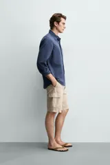Bermuda cargo regular fit color beige, confeccionada en mezcla de algodón y lino con efecto lavado. Cuenta con bolsillos laterales tipo cargo con solapa en las perneras, bolsillos frontales, cierre frontal con cremallera y botón, y presillas para cinturón.