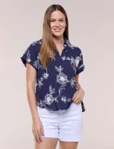 Blusa azul marino de corte amplio en tejido de puro algodón, con cuello camisero abierto en V y detalle de bordado floral en color blanco en toda la superficie. Cuenta con mangas cortas de hombro caído con puño doblado fijo y ruedo curvo con espalda más larga.