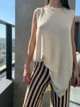 Chaleco de punto color beige, sin mangas, con cuello redondo y diseño asimétrico de corte holgado.