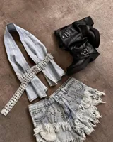 Top tipo halter confeccionado en denim claro, con diseño de tiras largas que se cruzan y se ajustan mediante un cinturón integrado con múltiples ojales metálicos.
