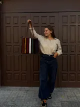 Cartera tipo tote de cuero con diseño de franjas verticales multicolores en tonos tierra, rojo y azul. Cuenta con correas trenzadas de cuero y cierre superior.