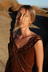 Vestido midi de gamuza color marrón cognac, con escote en V y detalles de calados geométricos artesanales en rombos. Presenta costuras decorativas con ribetes de cuero metalizado en tono cobre.