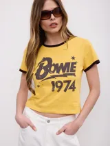 Remera amarilla de manga corta estilo ringer, con cuello y bordes de mangas en contraste color marrón oscuro. Presenta estampado frontal con la inscripción "Bowie 1974" y detalles de estrellas.