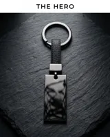 Llavero de diseño rectangular con chapa metálica en color negro pulido y correa de cuero sintético negro. Cuenta con una argolla circular metálica para sujetar llaves.