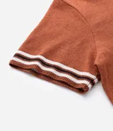 Camisa de punto jacquard color naranja, con cuello solapa, manga corta y cierre frontal con botones. Presenta detalles de rayas horizontales en contraste en el ruedo y en los puños de las mangas.