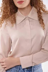 Camisa color beige con cuello clásico, cierre frontal con botones y detalle de flecos metálicos en el cuello.