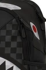 Mochila Sprayground negra con estampado a cuadros grises y blancos, diseño de boca de tiburón con dientes blancos y encías rojas.