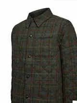Chaqueta de lana Harris Tweed con patrón de tartán en tonos verdes, marrones y detalles en burdeos. Presenta cuello camisero, cierre frontal con botones, bolsillos de parche y acolchado interior térmico.