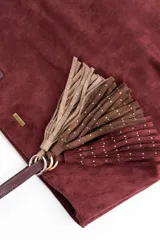 Charm para bolso compuesto por flecos de cuero sintético color marrón, decorados con pequeñas tachas metálicas doradas. Incluye un aro y un cierre de mosquetón metálico en tono dorado.