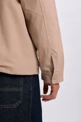 Campera color taupe con cuello de pana marrón oscuro, cierre frontal y botones a presión. Cuenta con dos bolsillos frontales con solapa.