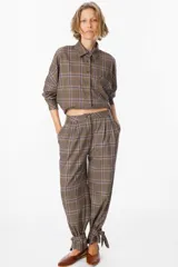 Pantalón de tiro medio con estampado a cuadros, corte holgado y pinzas en la cintura. Presenta un diseño distintivo con tiras ajustables en los tobillos que permiten crear un efecto fruncido.