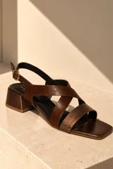 Sandalias de cuero vacuno color beige, con diseño de tiras cruzadas en el empeine, puntera cuadrada, taco bloque mediano y tira ajustable con hebilla en el talón.