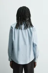 Camisa de corte regular confeccionada en tejido de algodón con efecto lavado. Presenta cuello solapa, cierre frontal de botones, manga larga con puño abotonado y un bolsillo de plastrón en el pecho.