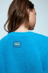 Cardigan corto de punto color rojo, con cierre frontal y cuello redondo. Presenta una textura acanalada y mangas largas.