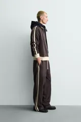 Sudadera de corte relajado en color azul marino con cuello alto y cierre frontal de cremallera. Presenta bandas laterales en color crema a contraste que recorren las mangas, puños y bajo en tejido rib, y bolsillos laterales de vivo.