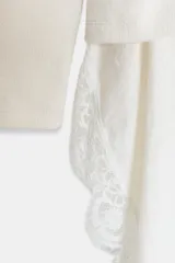 Camiseta color crudo de cuello redondo y manga larga, con detalle de aplicación de tejido lencero asimétrico a tono en el ruedo.