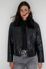 Chaqueta de efecto cuero brillante con acabado charol, cuello con solapas de piel sintética, cierre frontal con botones y bolsillos laterales.