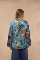 Camisa de satén azul con estampado botánico y floral en tonos amarillos, naranjas y blancos, de manga larga y cierre frontal con botones.