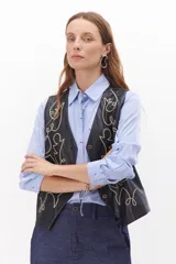 Chaleco marrón de simil cuero con bordado en color crema, cuello en V y cierre frontal con botones.