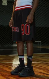 Bermuda deportiva negra de estilo NBA, confeccionada en tejido de punto deportivo. Presenta un elástico en la cintura con franjas rojas y blancas. Estampado frontal con la palabra "RAVERS" y el número "90" en rojo con borde blanco.