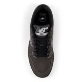 Championes New Balance modelo 480, color marrón oscuro con detalles en negro y blanco. Confeccionados en gamuza, cuero y malla, con logo "N" característico en los laterales. Inspirados en los zapatos de baloncesto clásicos de las décadas de 1980 y 1990.