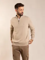 Sweater de punto en color beige, con diseño de medio cierre frontal, cuello alto y puños y ruedo acanalados. Presenta un pequeño bordado en el pecho.