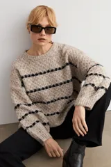 Sweater de punto con textura, color beige melange con rayas horizontales negras. Presenta cuello redondo, mangas largas y corte holgado.