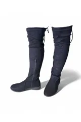 Bota bucanera de gamuza marrón, de caña alta elástica por encima de la rodilla, punta redondeada, suela plana y cierre lateral interno.