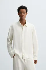 Camisa de corte relajado confeccionada en tejido de cáñamo, color blanco. Presenta cuello de solapa, manga larga con puños abotonados y cierre frontal de botonadura.