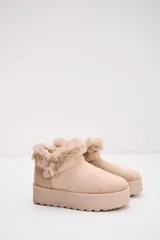 Bota corta tipo moon boot color beige, confeccionada en gamuza sintética con interior y borde superior de piel sintética. Presenta una suela de plataforma plana y una tira decorativa con hebilla metálica en el lateral.
