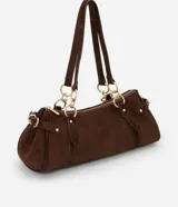 Cartera mediana de diseño alargado y estructura firme, confeccionada en gamuza sintética de color marrón. Cuenta con doble asa fina sujeta por argollas metálicas doradas, cierre superior y detalles de solapas decorativas con tachas en los laterales.